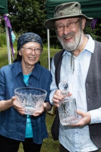 Sandy & Roger Clubley smiling while holding an engraved fruit bowl and decanter, following the awards presentation