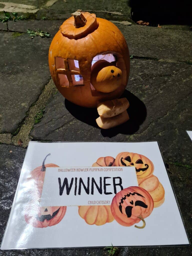 Winning child pumpkin with the winner's certificate - a large pumpkin with a window and doorway cut out, with some pumpkin slice steps and a happy little pumpkin wedged in the doorway.