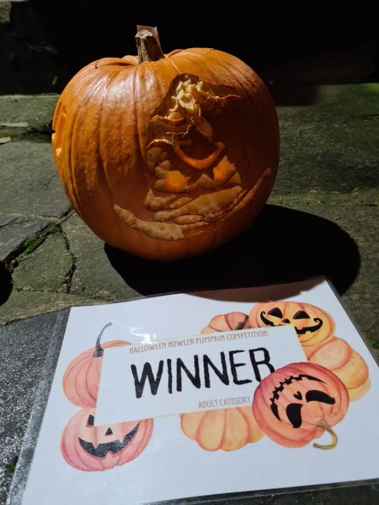 Adult winner's pumpkin with the winning certificate. The pumpkin has intricate carvings of the sorting hat from Harry Potter, with piercing orange eyes.