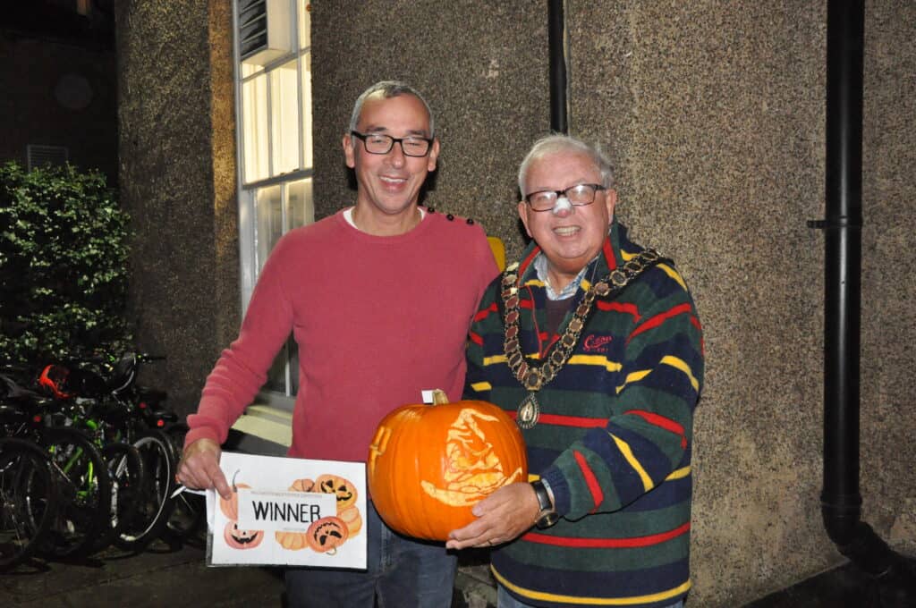 The Mayor of Sedgefield Peter Hinde standing with Adult pumpkin competition winner Jason, displaying the winning pumpkin and certificate. The pumpkin has intricate carvings of the sorting hat from Harry Potter, with piercing orange eyes, alongside the Harry Potter logo.